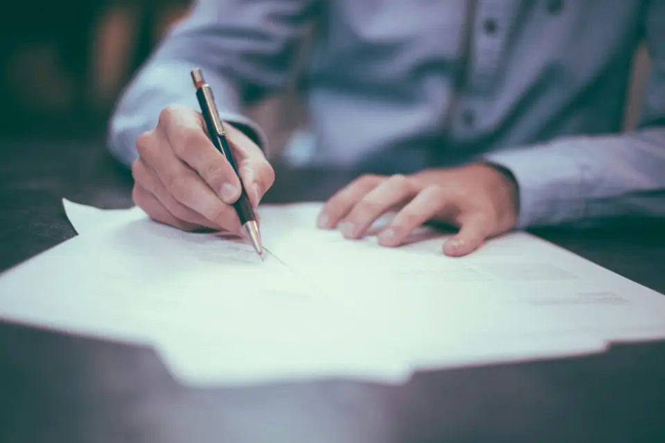 A person signs a document with a pen